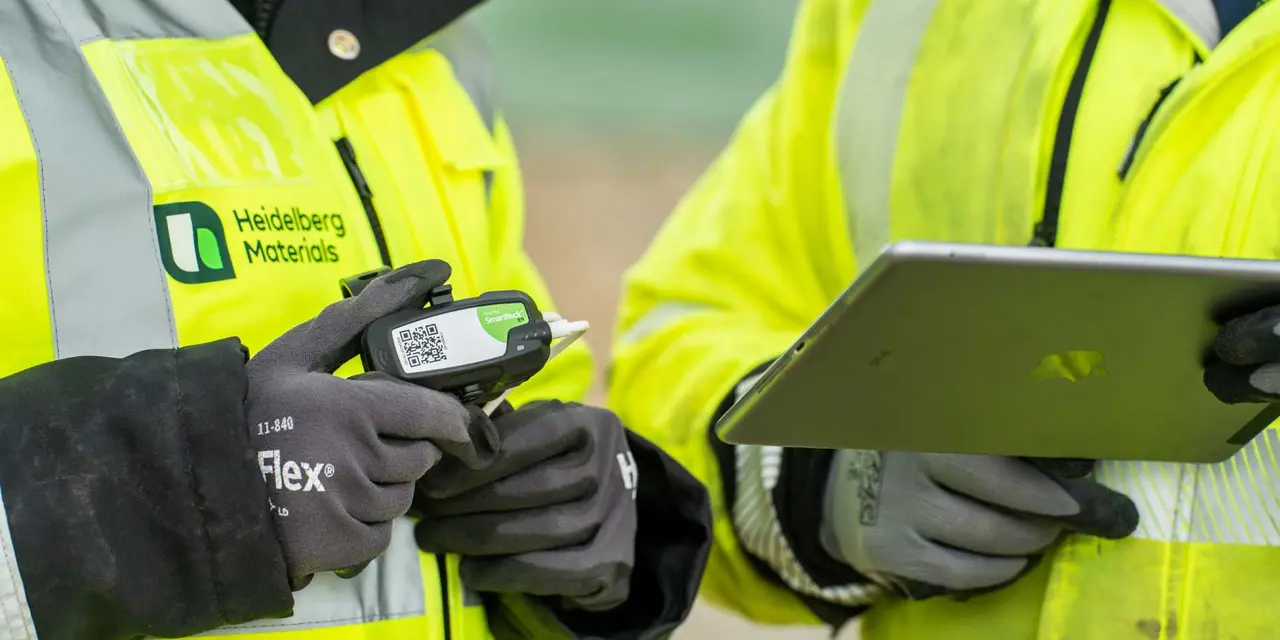 Two workers in high-visibility jackets use a handheld device and a tablet for monitoring operations.