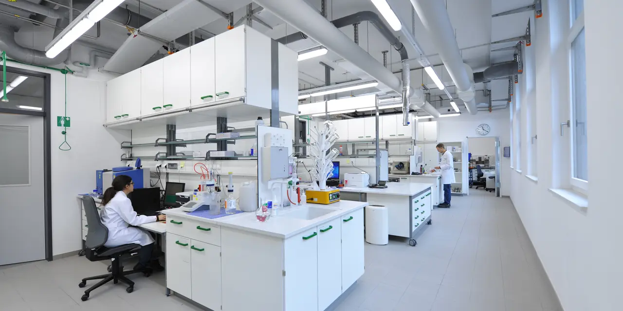 Chemistry lab with tables and cabinets, people in lab clothes standing and sitting