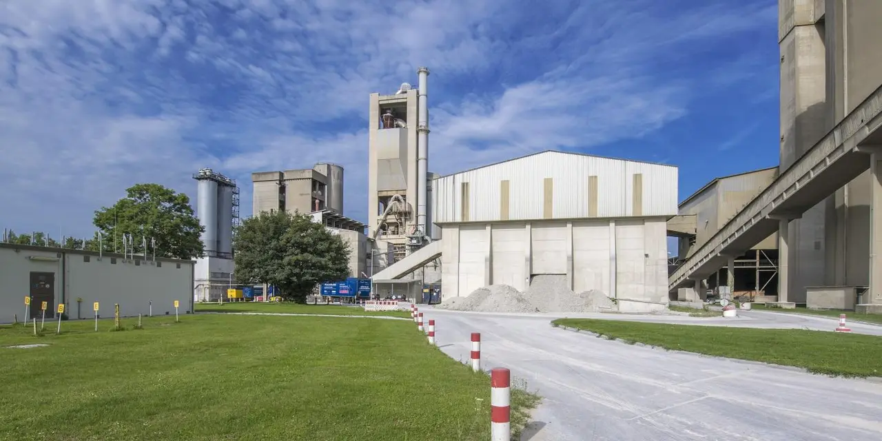 View of a large industrial complex with multiple silos and buildings under a blue sky, road leading to the facility on the left.