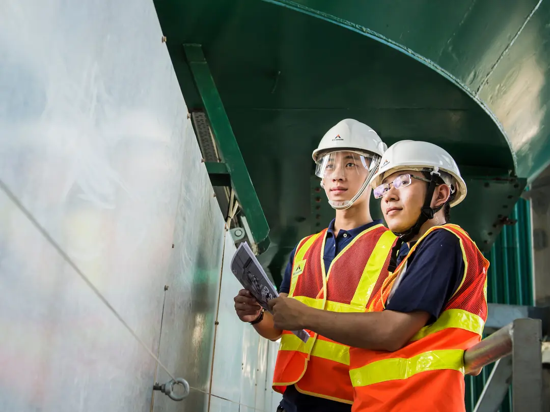 Two asian construction workers with white helmets examine a metal wall