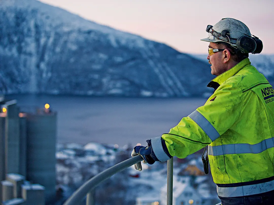 Ein Mann mit einer gelben Weste schaut auf das Zementwerk unter ihm