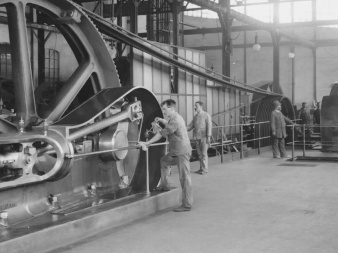 In an industrial hall workers are working on a steam engine