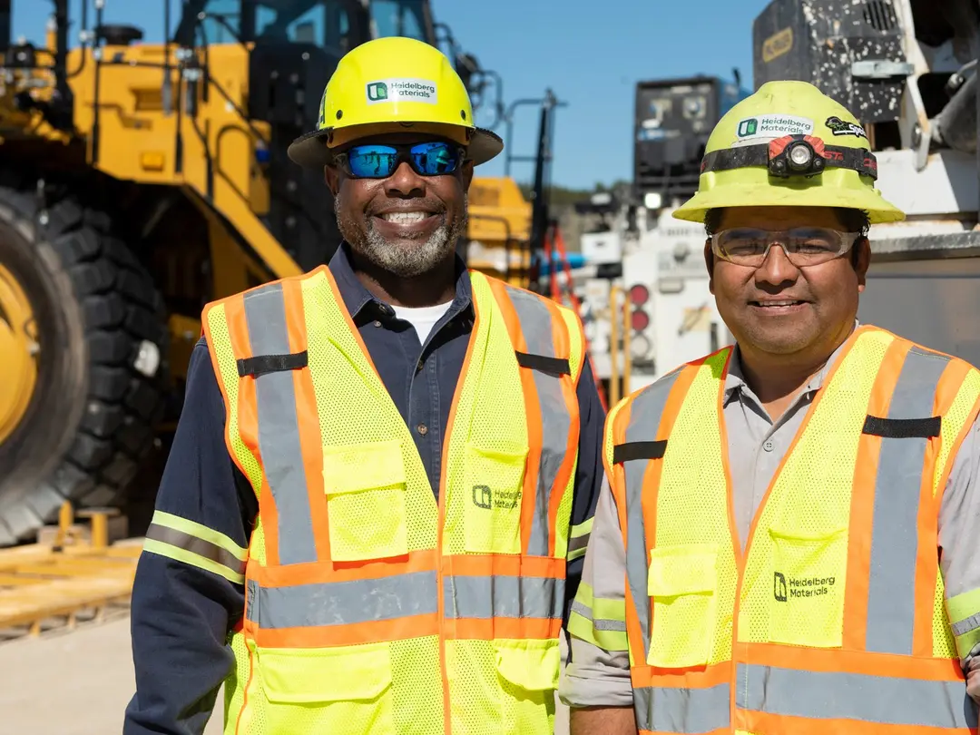 Two employees with helmets in front of gravel mountains