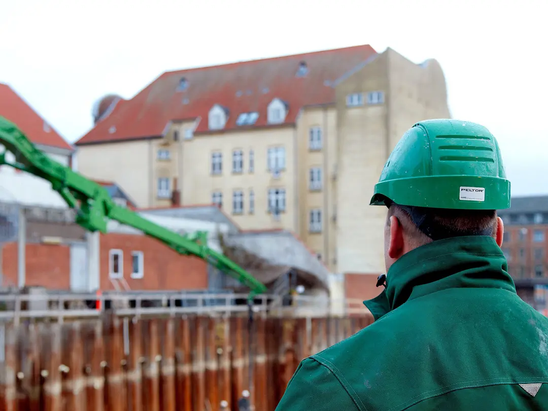 Ein Mann, der der Kamera den Rücken zuwendet, blickt auf eine Baustelle in einer Stadt