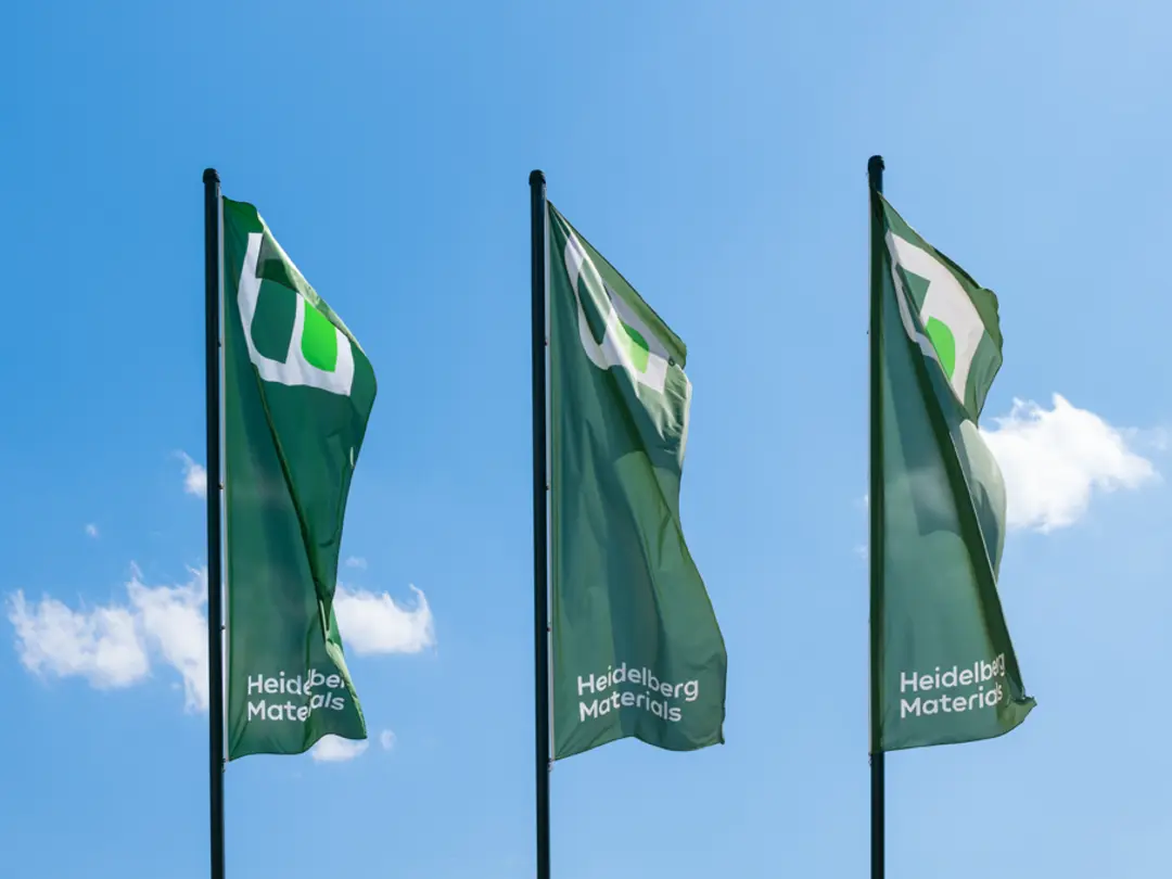 Drei grüne im Wind wehende Fahnen mit dem Heidelberg-Materials-Logo