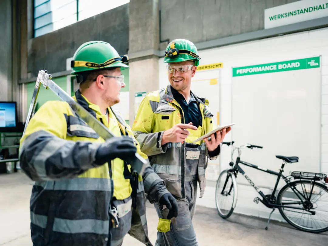 Zwei Männer in Schutzkleidung laufen durch ein Zementwerk, einer davon hält ein Tablet