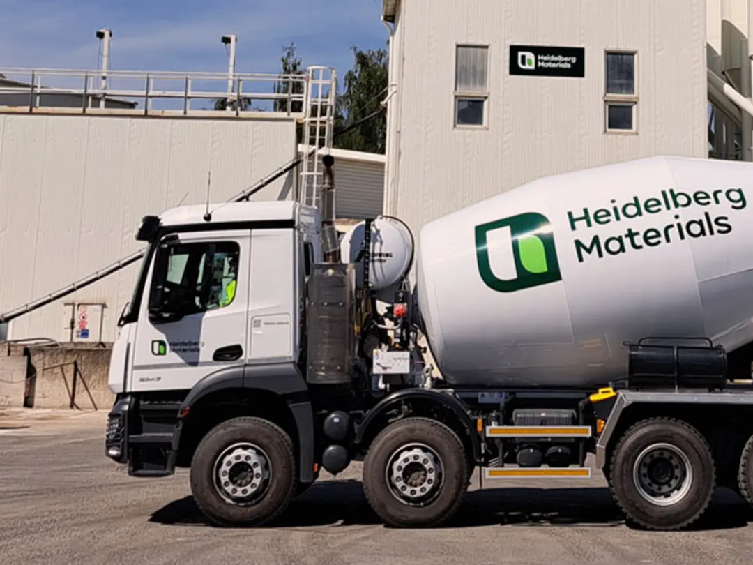 Ein Fahrmischer von Heidelberg Materials parkt auf vor einem Werk an einem sonnigen Tag.