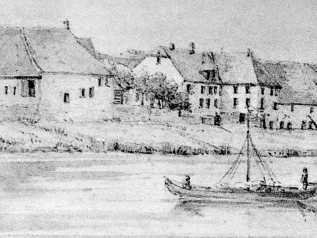 A black and white drawing of a historical settlement on the bank of a river. Several buildings with gabled roofs are visible, as well as a sailing boat on the river.