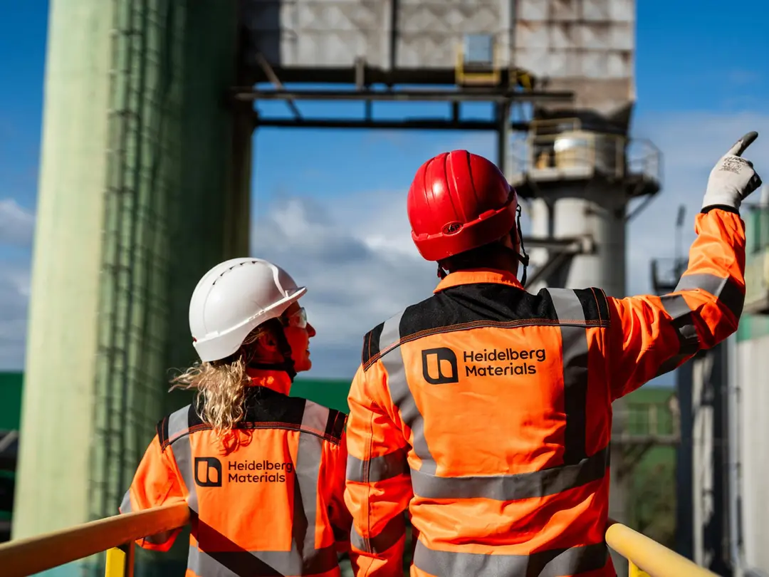 Rückansicht zweier Personen in Schutzkleidung in einem Zementwerk