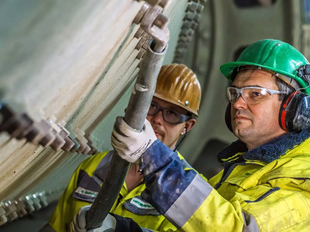 Zwei Personen in Schutzkleidung, einer davon arbeitet mit einem Werkzeug