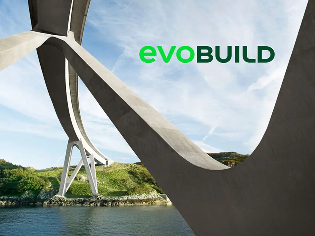 Bottom view of a modern bridge construction with curved concrete piers spanning a river landscape with green hills in the background. The "evoBuild" logo in green and black lettering at the top right.