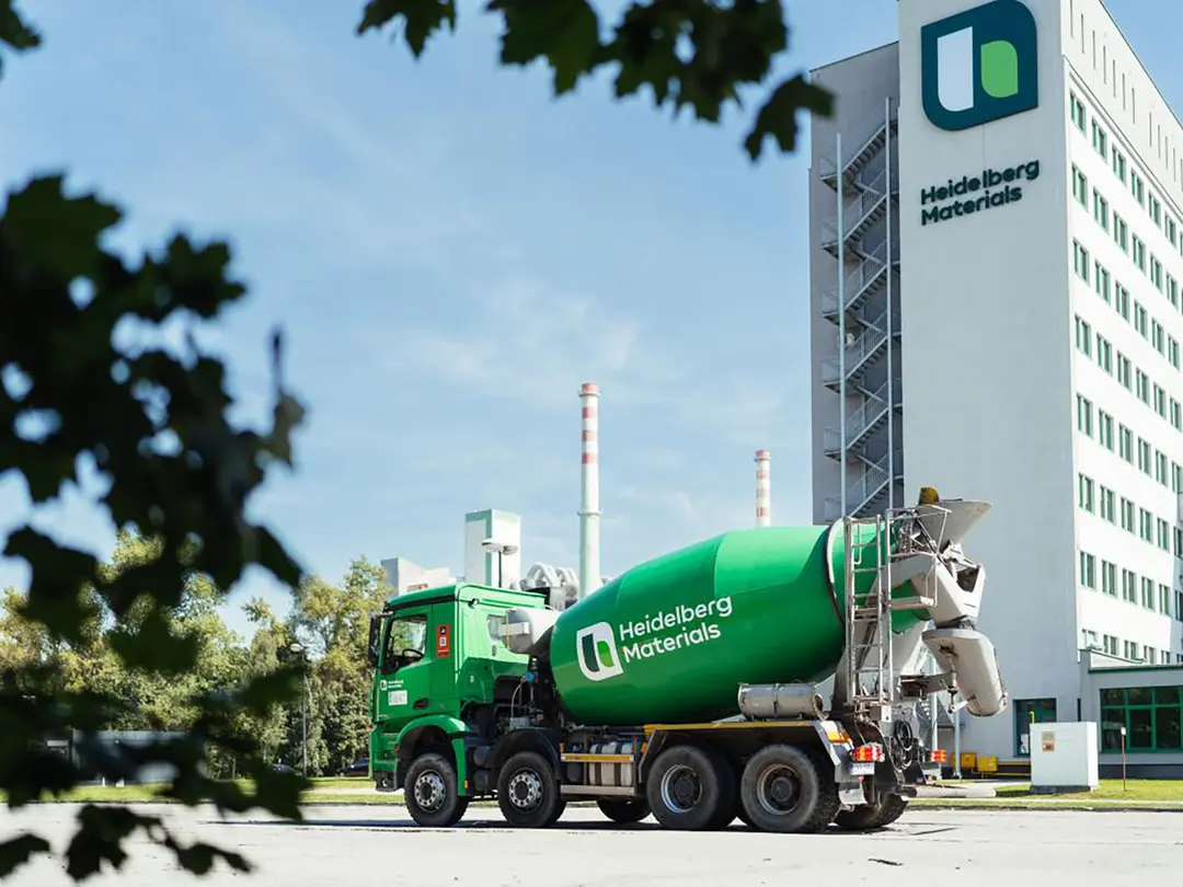 Grüner Fahrmischer vor einem mehrstöckigen Gebäude mit der Aufschrift „Heidelberg Materials“