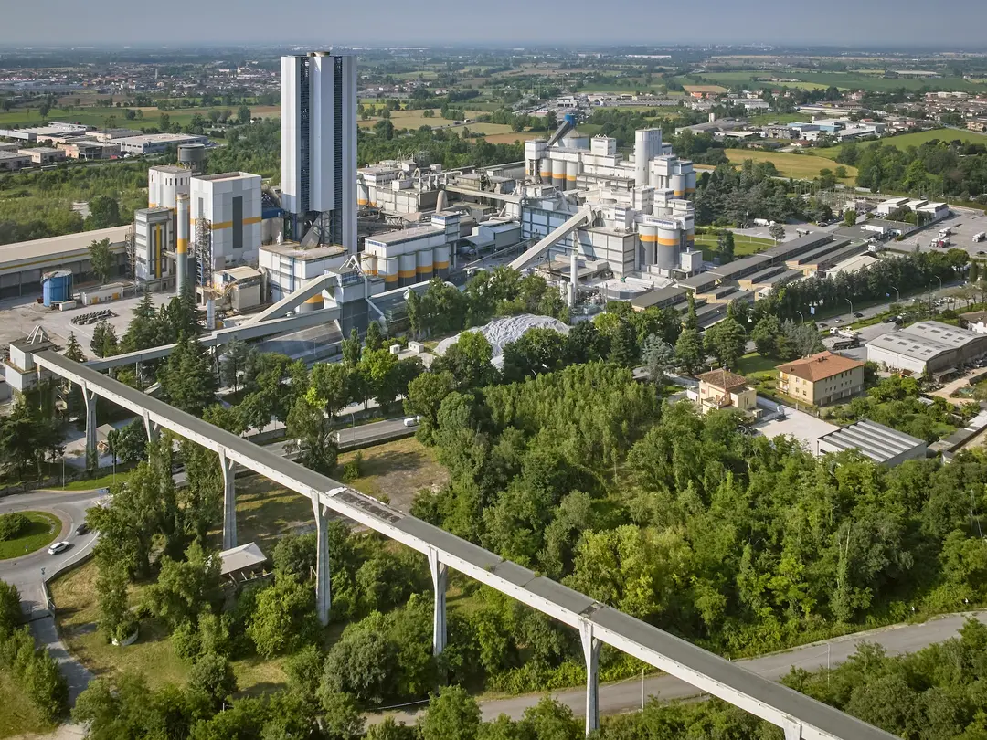 A cement plant surrounded by greenery and nearby infrastructure.