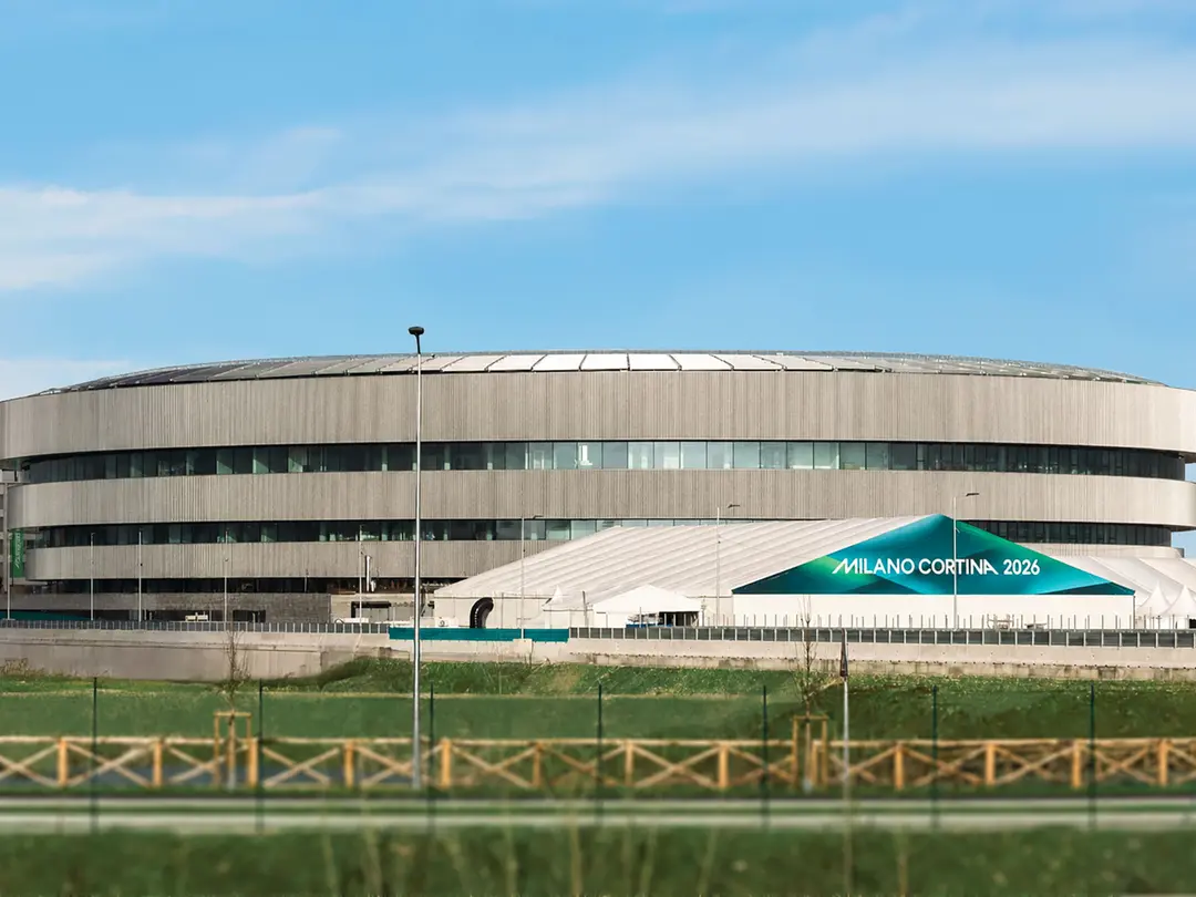 The Arena Santa Giulia, a modern circular building, surrounded by grass and fencing.