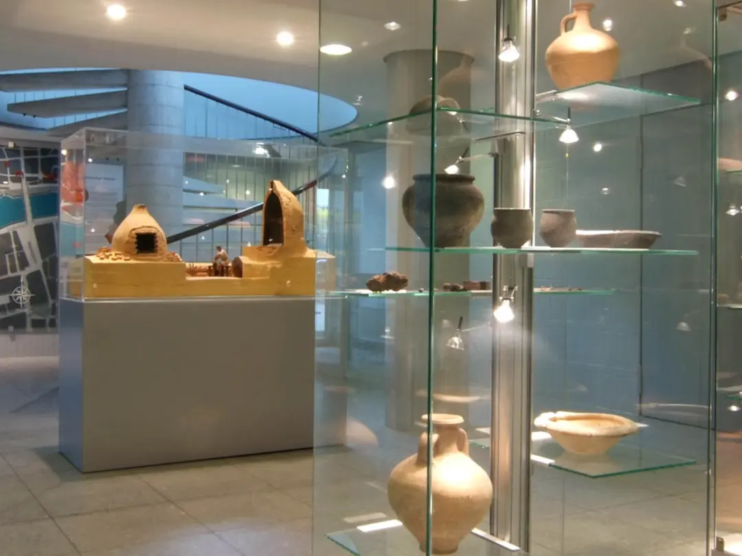 Raum mit Vitrinen, in denen Ausgrabungsgegenstände gezeigt werden, auf der Wand im Hintergrund eine Landkarte mit dem Neckar, daneben eine Wendeltreppe