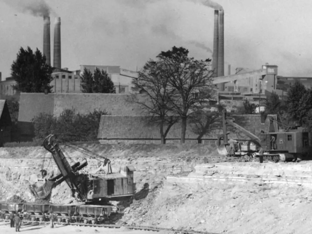 Historisches Foto eines Steinbruchs mit Baggern und Dampf-Güterzügen, im Hintergrund qualmende Schlote