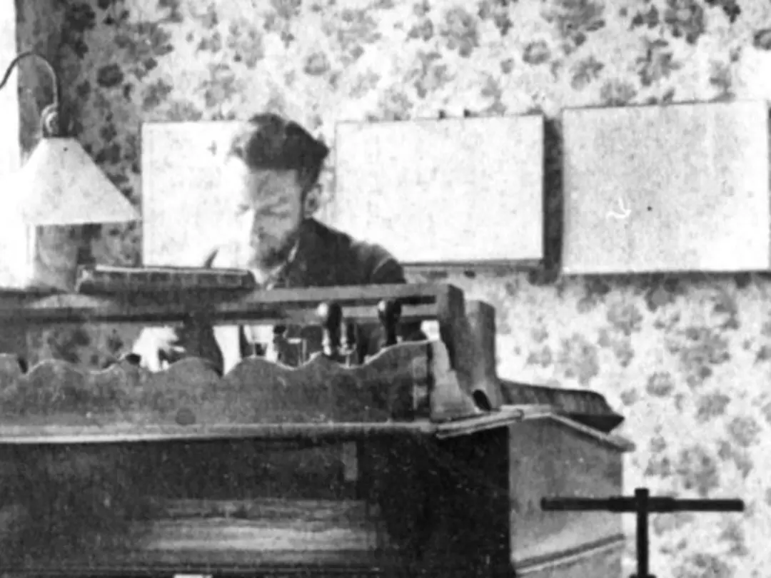 Black and white photo of a man sitting at a desk, another man sitting next to him