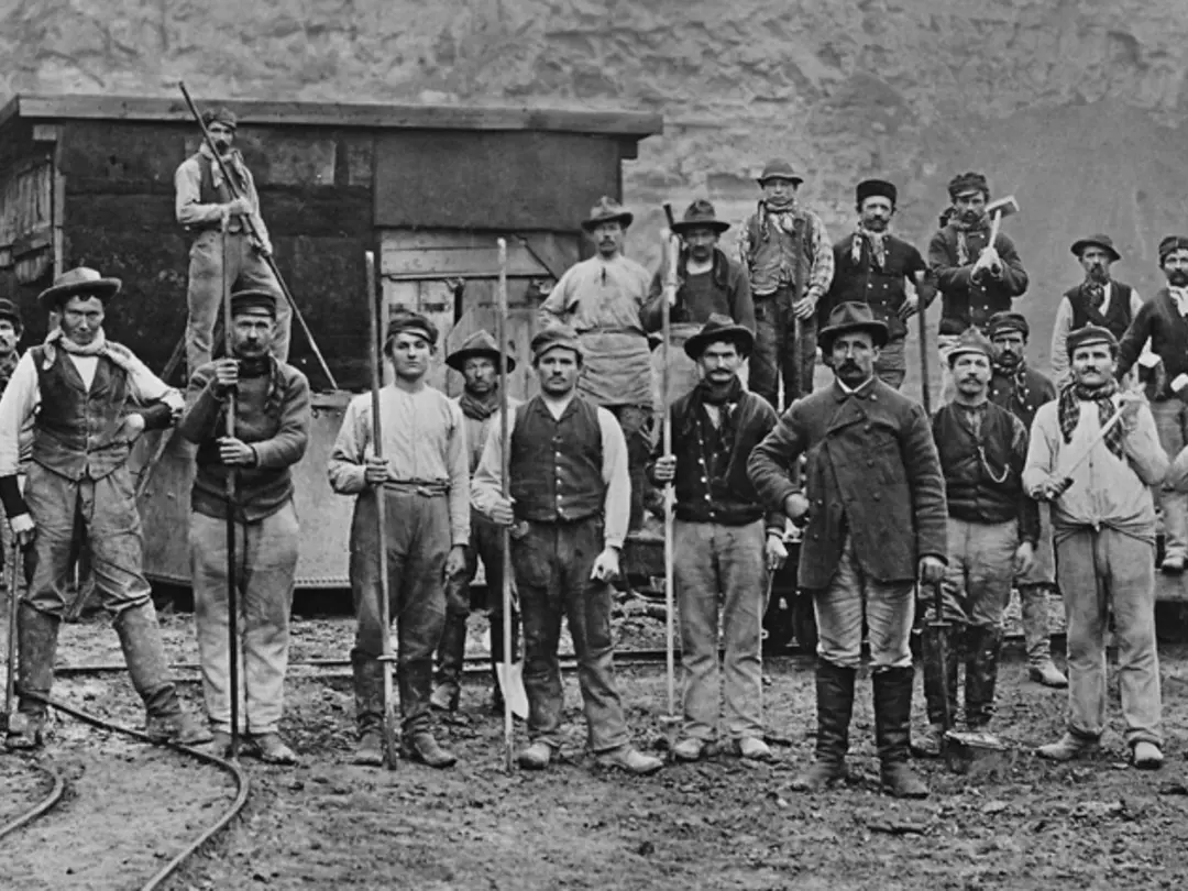 Historisches Foto; eine Gruppe von Männern mit Schaufeln und anderem Werkzeug steht vor einer Felswand in einem Steinbruch auf Schienen und schaut in die Kamera