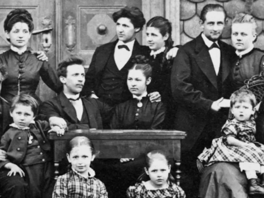 Black and white photo of a large family partly standing and partly sitting around a small desk