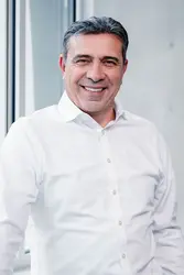 Ozan Kacar wearing a white shirt standing in front of a window, one hand on the windowsill