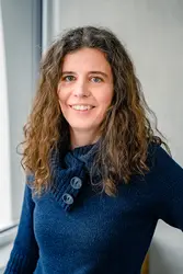 Eszter Harsányi in dunkelblauem Pullover vor Fensterfront und grauer Betonwand