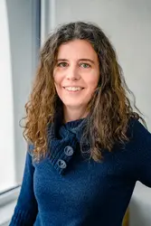 Eszter Harsányi in dunkelblauem Pullover vor Fensterfront und grauer Betonwand