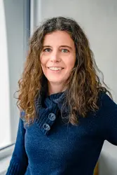 Eszter Harsányi in a dark blue jumper in front of a window and a grey concrete wall