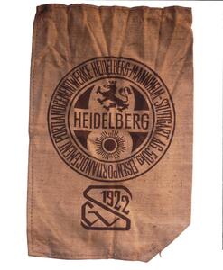A vintage burlap sack with the "Cementwerke Heidelberg-Mannheim" logo. The logo features a lion and the year "1922."