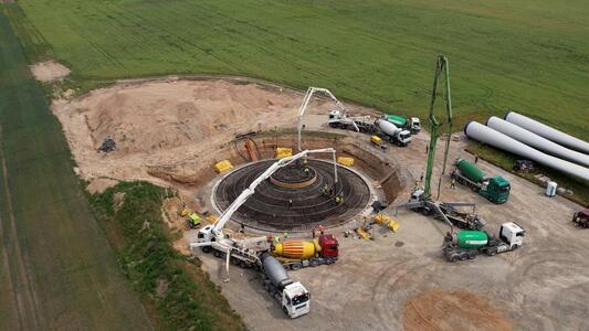 Blick von oben auf das kreisrunde Fundament eines Windrads, um das Betonpumpen stehen