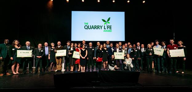 People are standing on a stage and holding posters, the posters show the prize money.