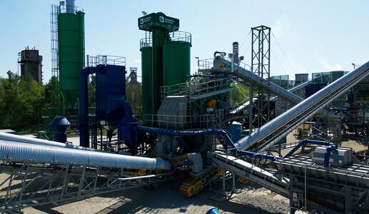 An industrial complex featuring large cylindrical storage tanks in shades of green and blue, surrounded by a complex network of metal pipes and structures under a clear sky