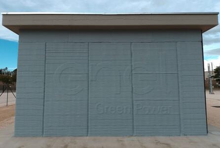 Eine 3D-gedruckte Seitenwand eines Gebäudes, die die einzigartige, geschichtete Textur der 3D-Drucktechnologie zeigt. Die Wand wirkt robust und ist vor einem Hintergrund mit bewölktem Himmel zu sehen. Der Aufdruck "Enel Green Energy" ist sichtbar.