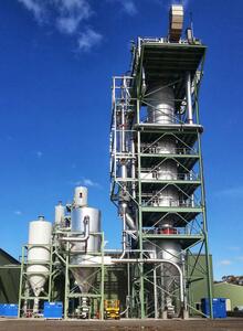 A large, industrial plant with a tall, multi-level part in the centre. Several smaller tanks and pipes are connected to the column.
