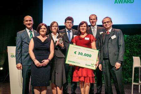 Seven people on a stage, one of them carrying a symbolic cheque for €30,000 with the words HeidelbergCement and Quarry Life Award written on it. 