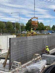 Baugrube, in der Betonwände und Stahlmatten stehen, darüber schwebt ein Behälter an einem Kran.