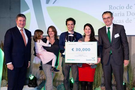 Sieben Personen auf einer Bühne, eines davon ist ein Kind auf dem Arm, eines ein Baby in einer Trage. Eine Person hält einen symbolischen Scheck mit dem Aufdruck 30.000 €, HeidelbergCement und Quarry Life Award.