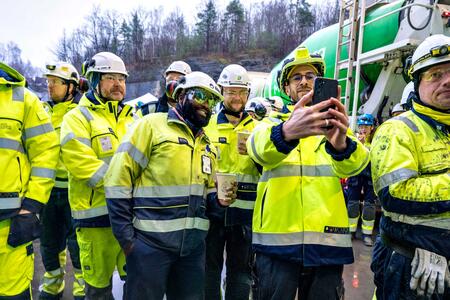 A group of people in protective clothing in front of a ready-mixed cement truck, with trees in the background. One of them is taking a selfie.