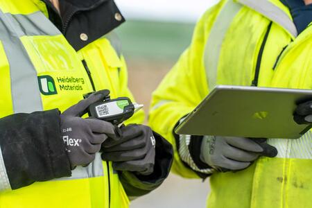 Two workers in high-visibility jackets use a handheld device and a tablet for monitoring operations.