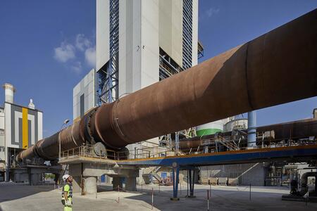 A large industrial cement kiln at a Heidelberg Materials facility with a worker in safety gear standing nearby.