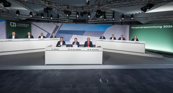 Vorstand von Heidelberg Materials bei der Hauptversammlung 2026 an weißen Tischen in einem modernen Konferenzraum.