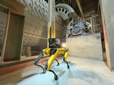 A yellow robotic dog stands in a cement plant with machinery in the background.