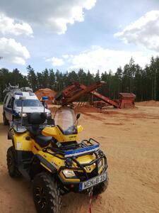 Two special vehicles on the site of a gravel works, with conveyor belts and forest behind them.