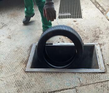 A worker disposing of a used tire into an industrial material intake opening.