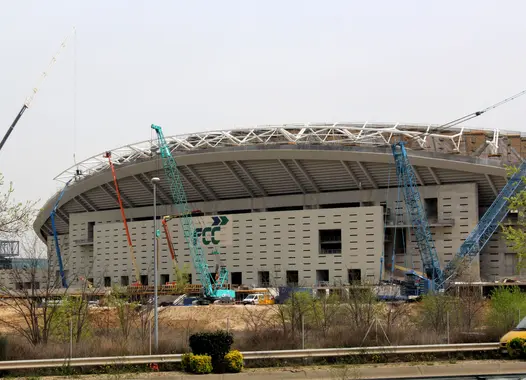 Expansive construction site of a large stadium, showcasing the intricate network of cranes and scaffolding under a clear sky