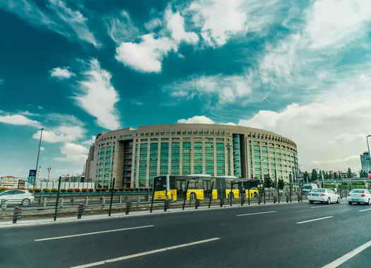 A modern circular building with a yellow tram passing by under a cloudy sky