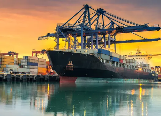 Cargo ship at port with cranes and containers during sunset