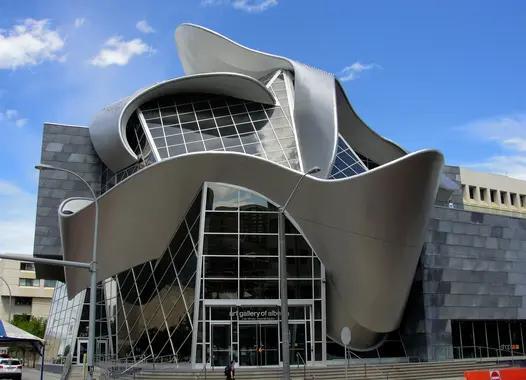A modern art museum with a distinctive architectural design featuring metallic curves and glass elements under a blue sky with clouds