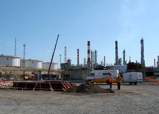 An industrial setting with multiple large cylindrical storage tanks and tall chimneys emitting no visible emissions against a clear sky.