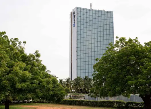 A tall glass building with the logo of Radisson at the top. The building is surrounded by greenery, with trees in the foreground framing the view.