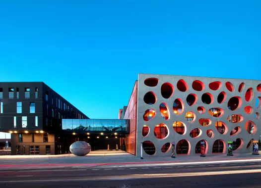 A modern building with a striking facade featuring large, circular cutouts. The building is illuminated against a dark blue sky.